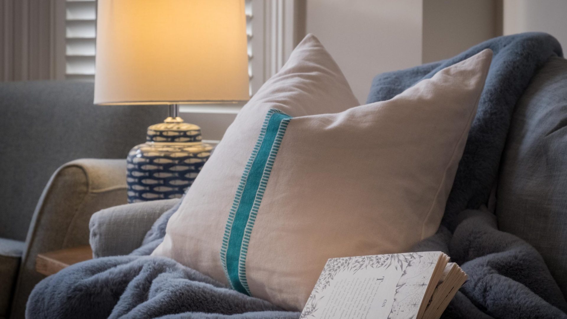 sofa cushion with lamp, cosy blanket and book in a Seaview holiday home